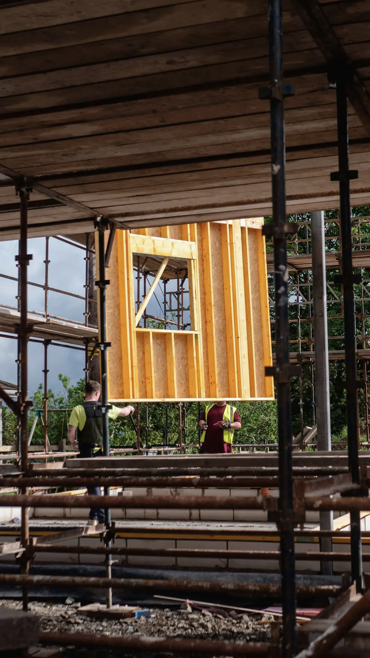 Two workers guiding a prefabricated wood wall panel into place from a scaffold