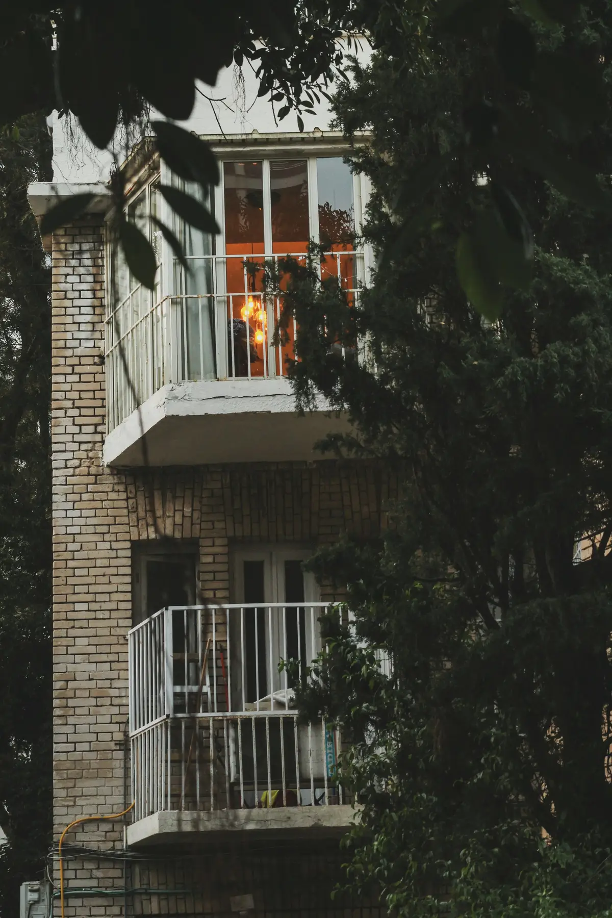 A white brick building with a small balcony behind trees